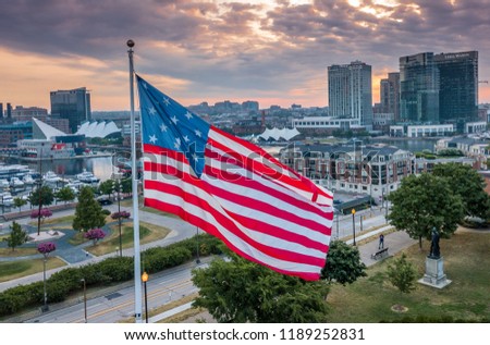 Proudly flying waving American flag over Federal Hill, Baltimore Inner Harbor with cloudy sunrise sky
