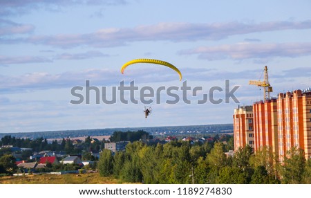 Flight of  motor paraplan.   man flies on  bright colorful motoparaplane above the village, field and construction site.
