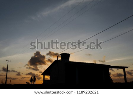 Silhouette of happy couple with a pet dog, next to the house and sunset in the background