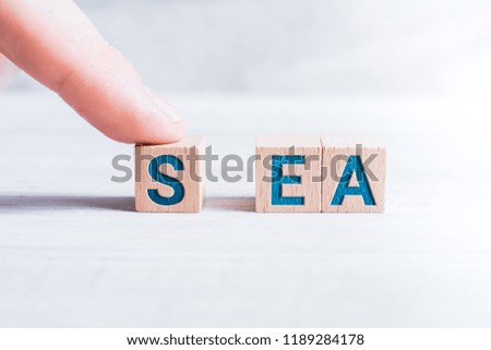 The Word SEA Formed By Wooden Blocks And Arranged By A Male Finger On A White Table