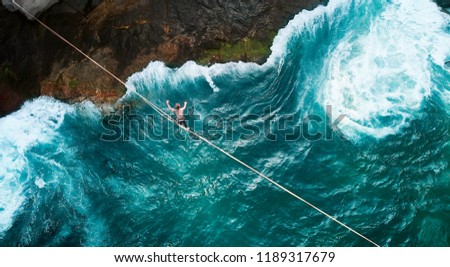 Aerial Drone Scenic Adventure Sport Portrait of a Mindfulness Slackliner Man Crossing a Tightrope in a Very Secret Cliff w. Giant Green Waves of Paradisiac Atlantic Ocean Rare Beach Next Vidigal Slum Royalty-Free Stock Photo #1189317679
