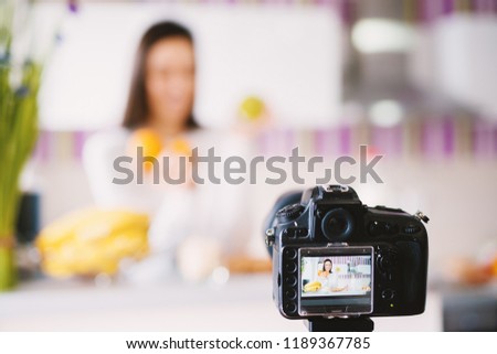 Camera taking picture of a charming young lady holding fruit.