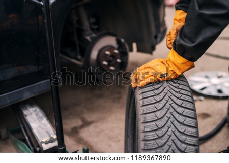 Picture of auto mechanics hands putting car tire on cr in workshop.