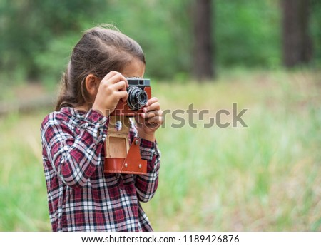 Small girl with camera is taking pictures of nature. Young photographer.
