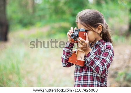 Small girl with camera is taking pictures of nature. Young photographer.