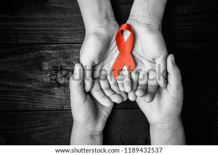 AID red ribbon in hand on a black wooden background, a symbol of the fight against HIV, AIDS and cancer. concept of helping those in need. black and white. Royalty-Free Stock Photo #1189432537