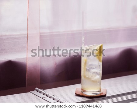 Ice lemonade placed by a window with purple curtains. close up
