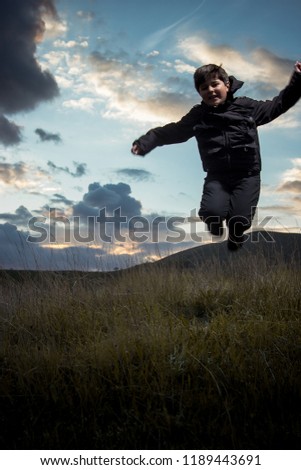 child jumping against the background of the evening cloudy skyline.