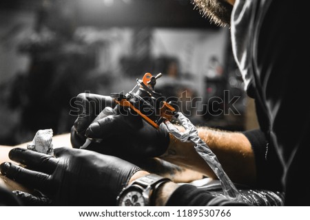 The tattoo artist creates a picture on the body of a man. close-up of tattoo machines and hands