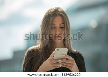 Attractive woman is sitting on the windowsill and uses a smartphone.