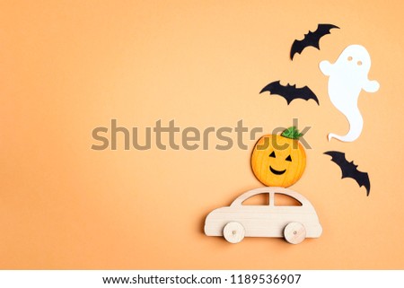 Wooden toy car with funny pumpkin on the roof and bats on orange background. Space for text. Flat lay Halloween background.