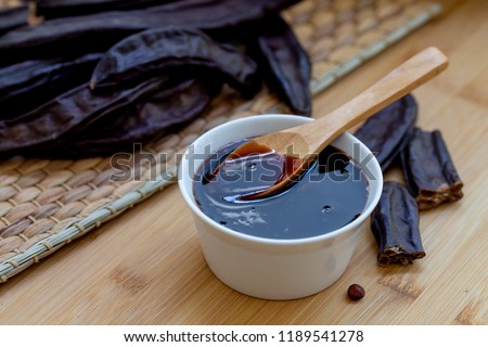 Carob molasses and carob pods on wooden background Royalty-Free Stock Photo #1189541278