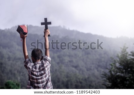 Boy holding Bible and christian Cross with mountain background. young christian concept