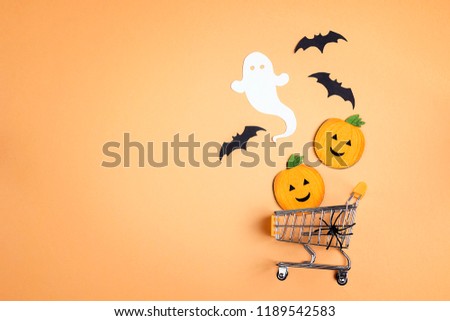 Shopping trolley with decorative pumpkins, ghost, bat and copy space on orange backdrop. Flat lay Halloween background. Halloween sale concept.