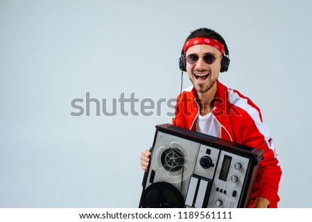 cheerful fashionable man wearing a red sports suit and headphones dancing jumps with a retro tape recorder. interesting and fervent style of the 90s.