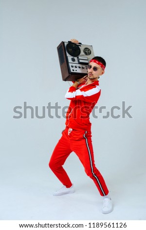 cheerful fashionable man wearing a red sports suit dancing jumps with a retro tape recorder. interesting and fervent style of the 90s. Royalty-Free Stock Photo #1189561126