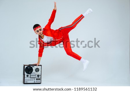 cheerful fashionable man wearing a red sports suit dancing jumps with a retro tape recorder. interesting and fervent style of the 90s. Royalty-Free Stock Photo #1189561132
