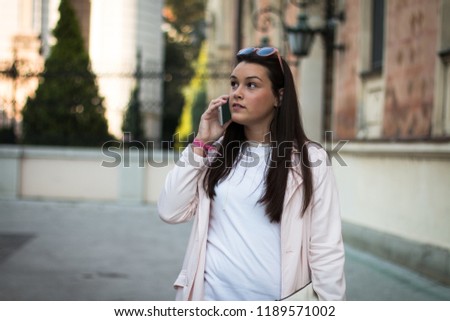 Young casual woman talking on smartphone outdoors on the street.