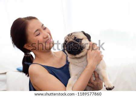 Beautiful Asian young woman playing with her dog and smile with dog pug breed looking in funny and serious face in bedroom feeling so happiness and relaxation,Dog Friendship Concept