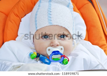 Beautiful little toddler boy with pacifier in white clothes sitting in orange stroller
