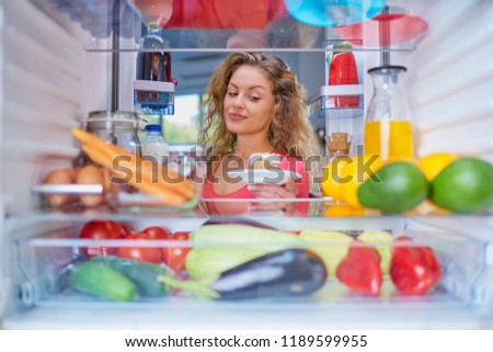 Woman breaking diet by taking cheesecake from fridge full of groceries. Picture taken from inside of fridge.