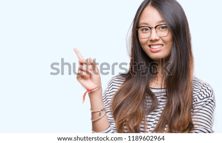 Young asian woman wearing glasses over isolated background with a big smile on face, pointing with hand and finger to the side looking at the camera.