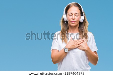 Middle age hispanic woman listening to music wearing headphones over isolated background smiling with hands on chest with closed eyes and grateful gesture on face. Health concept.
