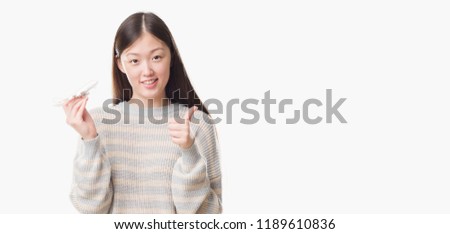Young Chinese woman over isolated background holding aircraft toy happy with big smile doing ok sign, thumb up with fingers, excellent sign