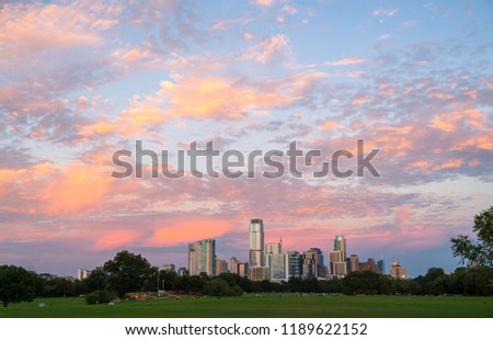 Zilker Park Sunset of amazing colors across the sky pinks and orange above a glowing Skyline Cityscape from the perfect view across green grass field in the large public park Iconic Landmark view