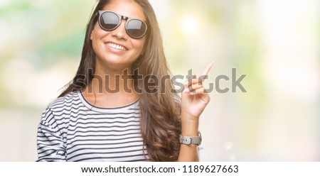 Young beautiful arab woman wearing sunglasses over isolated background with a big smile on face, pointing with hand and finger to the side looking at the camera.