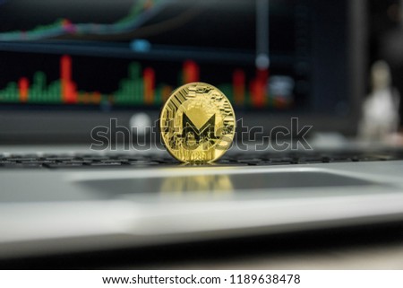 Golden coin of Monero on a black keyboard of silver laptop and diagram chart graph on a screen as a background. Cryptocurrency concept. Mining of ethereums online bussiness. Trading.