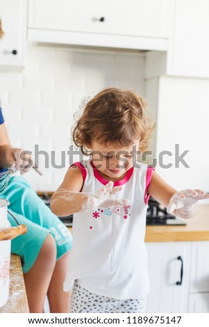 Brother and sister preparing dough for pancakes at the kitchen. Concept of food preparation, white kitchen on background. Casual lifestyle photo series in real life interior