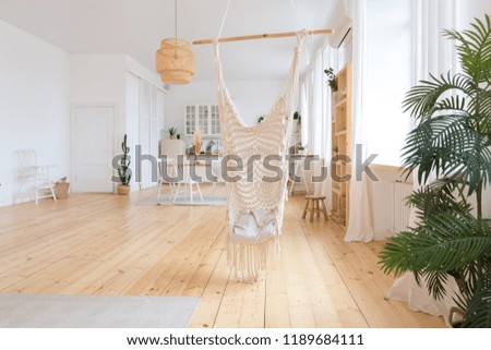 cute cozy light interior design of the apartment with a free layout of the kitchen and bedroom areas. a lot of windows, a wooden floor and a hanging swing.