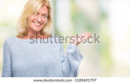Middle age blonde woman wearing winter sweater over isolated background smiling cheerful presenting and pointing with palm of hand looking at the camera.