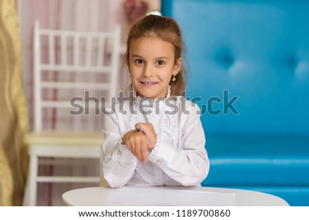 A cute little girl is sitting at a table drawing and telling something. The child is right in front of the camera smiling and looks happy.