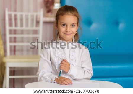 A cute little girl is sitting at a table drawing and telling something. The child is right in front of the camera smiling and looks happy.