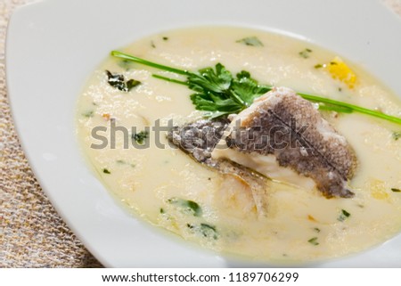 Picture of creamy soup with white fish hake served with  greens at plate