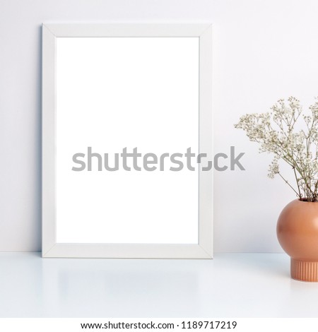 White mockup frame and white dried wildflowers in a brown vase on a shelf