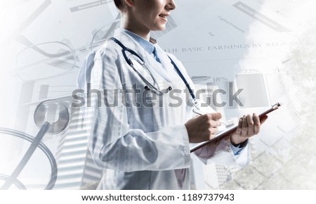 Side view of confident woman doctor in white medical uniform holding notebook and pen in hands while standing against city view and medical stuff on background.