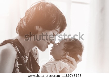 Asian Young Mother is happiness with his newborn baby at home, and kissing noses together. Add vintage style color  filter  and warm light.