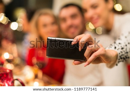 holidays, technology and people concept - close up of friends taking selfie by smartphone at christmas dinner