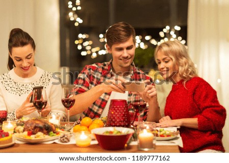 holidays and celebration concept - happy friends having christmas dinner at home and photographing food by smartphone