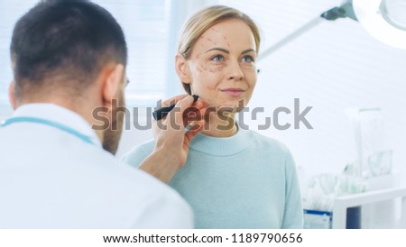 Over the Shoulder Shot of a Plastic / Cosmetic Surgeon Draws Lines on a Face of a Beautiful Female model for the Facelift Operation. Royalty-Free Stock Photo #1189790656
