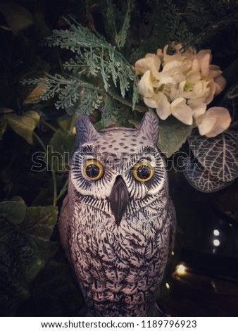 Halloween scene : Cute owl figure sculpture made from paper mache decorated with flower bouquet in vase and ornamental plants, vintage and shabby chic garden, vintage filter, soft focus, blurred image