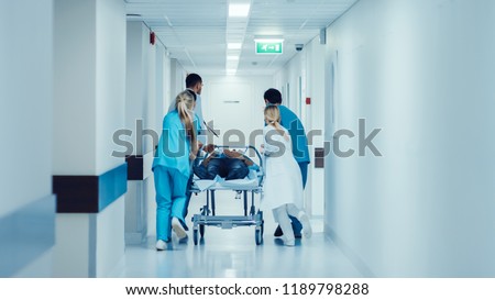 Emergency Department: Doctors, Nurses and Paramedics Push Gurney / Stretcher with Seriously Injured Patient towards the Operating Room. Bright Modern Hospital with Professional Staff Saving Lives. Royalty-Free Stock Photo #1189798288