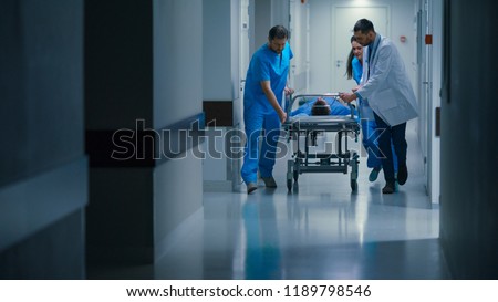 Emergency Department: Doctors, Nurses and Paramedics Push Gurney / Stretcher with Seriously Injured Patient towards the Operating Room. Bright Modern Hospital with Professional Staff Saving Lives. Royalty-Free Stock Photo #1189798546