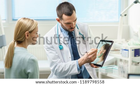 Plastic / Cosmetic Surgeon Consults Woman about Facial Lift Surgery, He Draws Arrows on Digital Tablet Computer Screen, Showing Types of Facelift and Nose Correcting Procedures Available for Her. Royalty-Free Stock Photo #1189798558