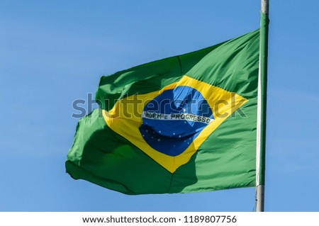 Flag of Brazil fluttering in the wind, old, with ragged edge, in blue sky background, presenting the words Order and Progress whole.
