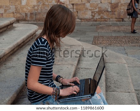 A teenage woman studying with a laptop on the stairs of a university in a university campus