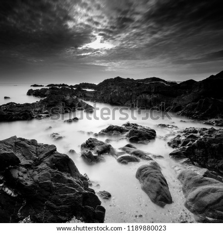 Long exposure seascape and rocky beach in black and white. A slow shutter speed was used to see the movement ( Soft focus due to long exposure shot ).